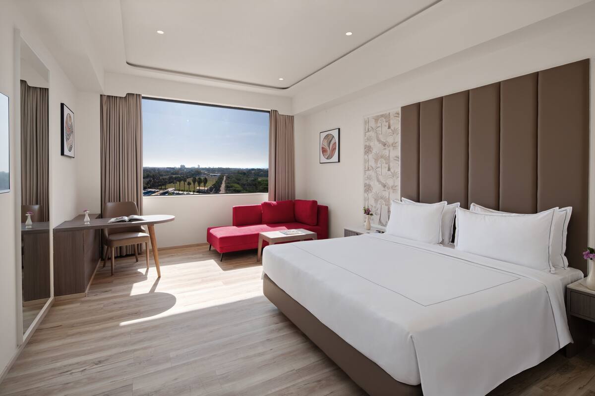 Ein modernes Hotelzimmer mit einem großen Bett, einem Schreibtisch, einer roten Couch und Blick auf die Stadt.