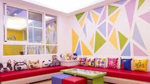 Una habitación luminosa y colorida con un sofá rojo, una mesa de vidrio y una pared con estampado geométrico.