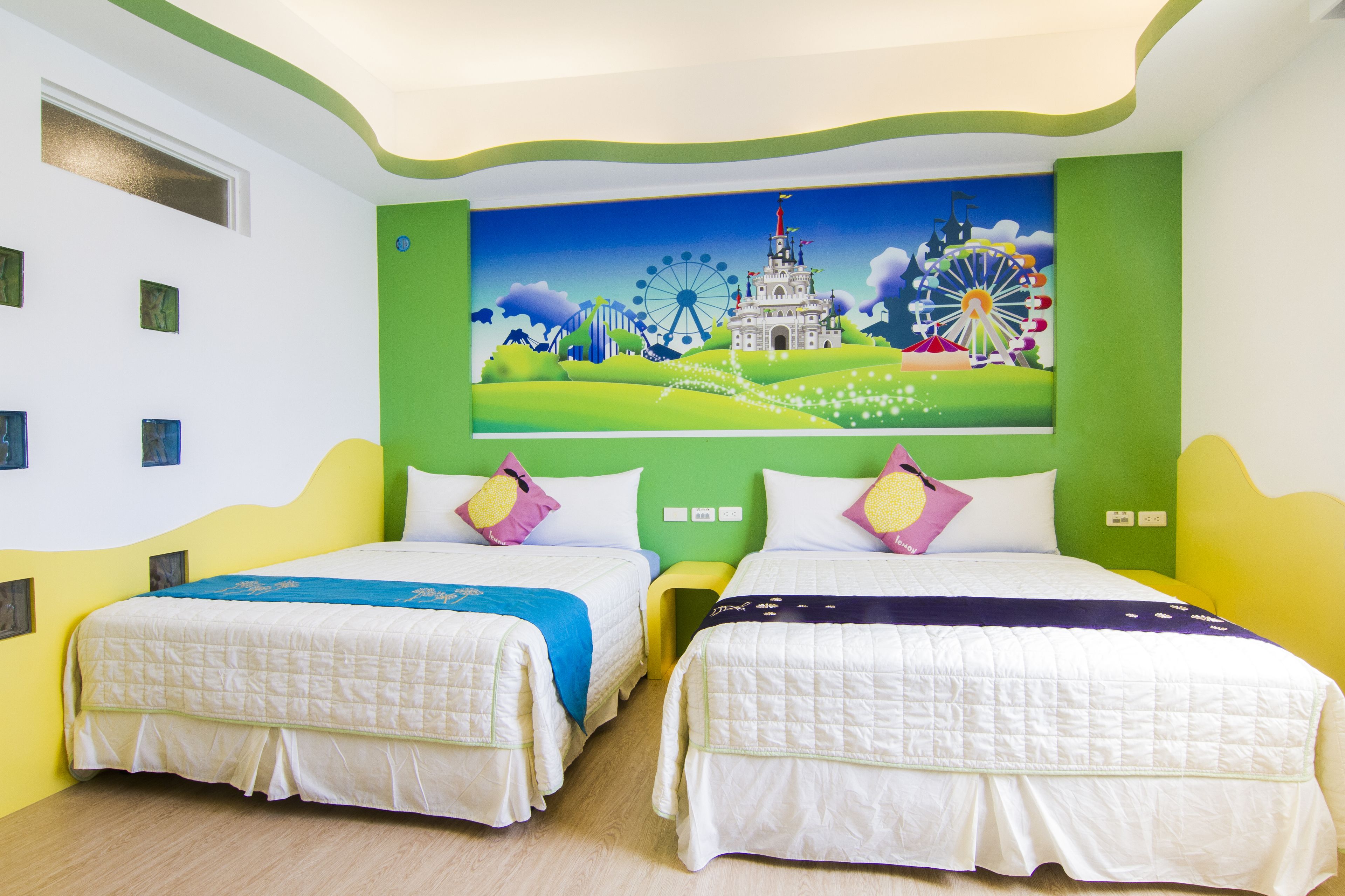 A room with two beds, a mural of a Ferris wheel and castle, and a green accent wall.
