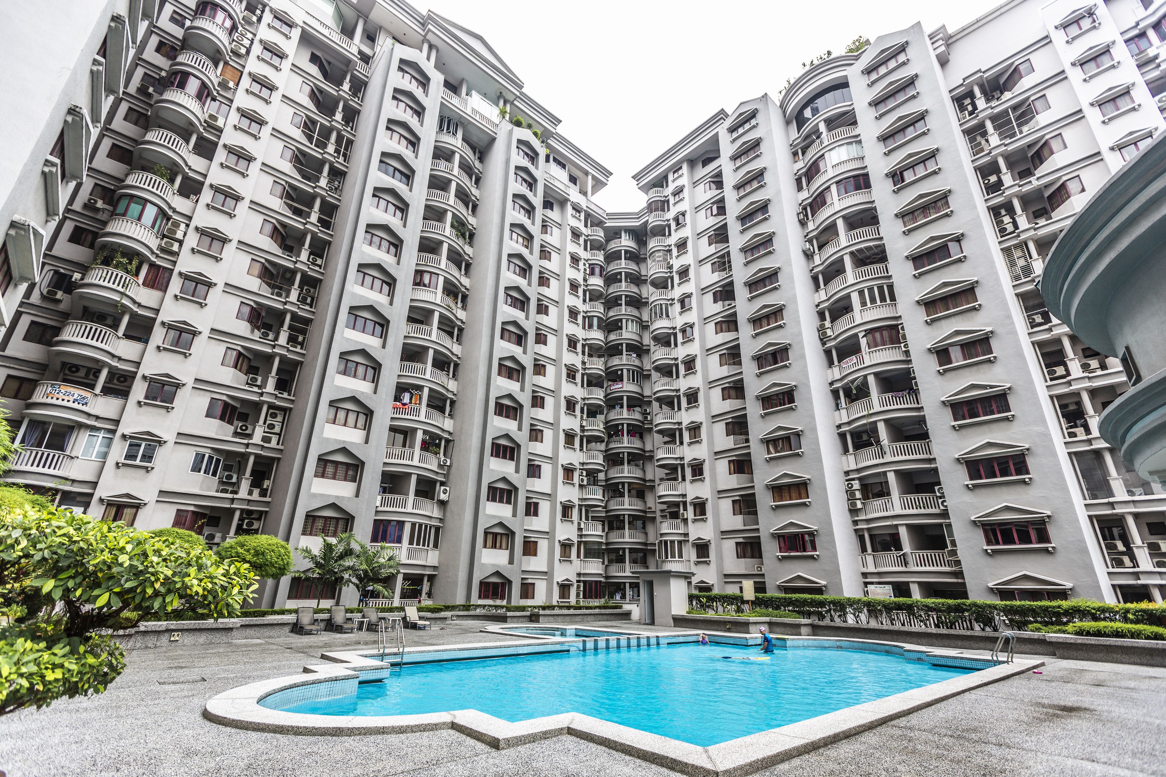 A high-rise residential building with multiple balconies and a swimming pool in the courtyard.