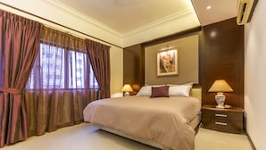 Une chambre d’hôtel avec un grand lit, deux tables de chevet avec des lampes, un tableau au mur et une fenêtre avec des rideaux.