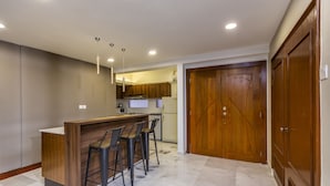 Une cuisine moderne avec un îlot central en bois et des tabourets de bar, un four encastré et une grande porte en bois.