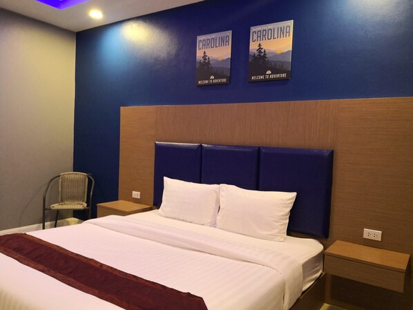 A hotel room with a large bed, two nightstands, a chair, and two wall posters of North Carolina.