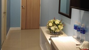 Un pasillo con puerta de madera, espejo, un jarrón de flores y agua embotellada sobre una encimera.