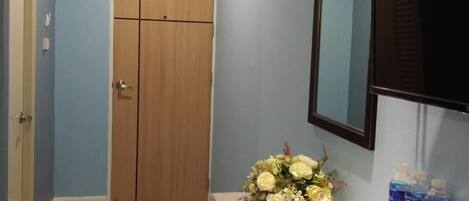 Un pasillo con puerta de madera, espejo, un jarrón de flores y agua embotellada sobre una encimera.
