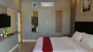 A modern hotel room with a large bed, a flat-screen TV, a desk with a computer, and a mirror.