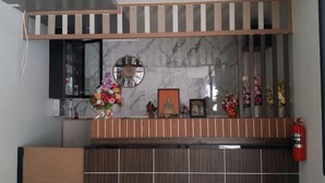 Un área de recepción con pared de mármol, un reloj y diversas decoraciones, incluyendo flores y una estatua de Buda.
