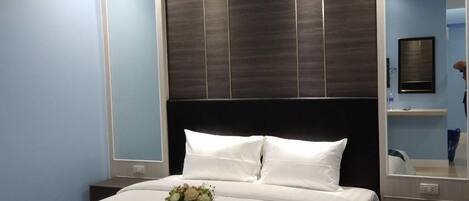 A modern hotel room with a large bed, a dark wood headboard, and a mirror above the bed.
