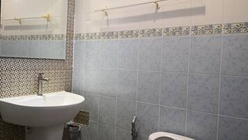 Un bagno con un lavandino bianco, un water e uno specchio. Sopra il lavandino e il water ci sono porta asciugamani.