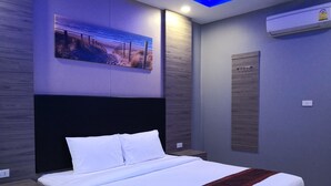 Un dormitorio moderno con una cama grande, una mesita de noche, un aire acondicionado de pared y un cuadro con una escena de playa.