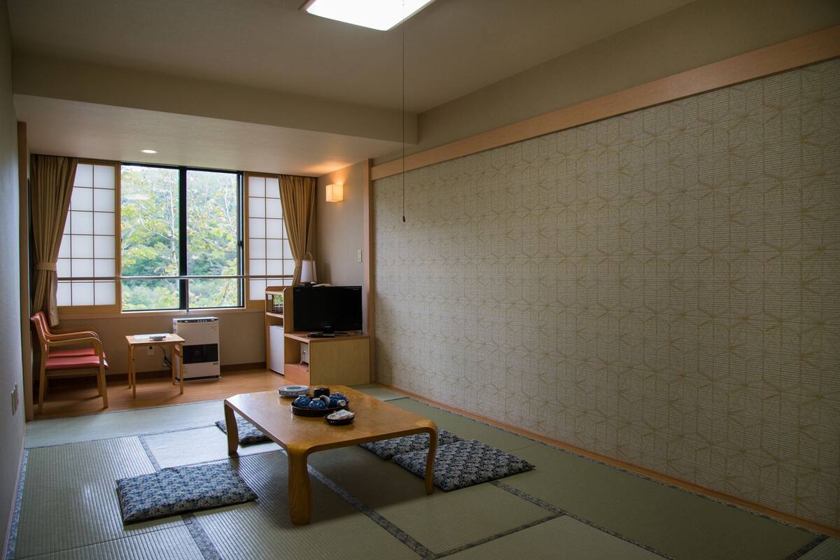 A traditional Japanese room with tatami flooring, a low table with a TV, a sofa, and a sliding door.