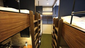 A narrow corridor with bunk beds on either side, a small table with a lamp, and a wall-mounted air conditioner. - Neighbors Kaede (Osaka)