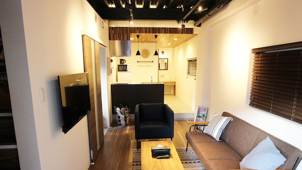 A modern living room with a sofa, a coffee table, and a TV mounted on the wall. - Neighbors Kaede (Osaka)