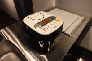 A rice cooker on a stainless steel countertop with a digital display and buttons. - Neighbors Kaede (Osaka)