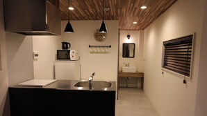 A modern kitchen with a stainless steel sink, a microwave, and a kettle on a white cabinet. There is a wooden ceiling with exposed beams and pendant lighting. - Neighbors Kaede (Osaka)