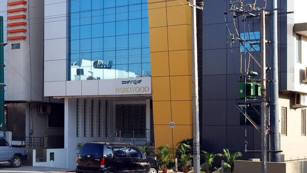 A modern building with a large glass facade, a sign reading "PARKWOOD," and a parked car in front. - Parkwood Suites (Bengaluru)