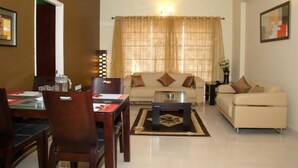 A living room with a sofa, coffee table, and dining area with chairs and a table. - Parkwood Suites (Bengaluru)