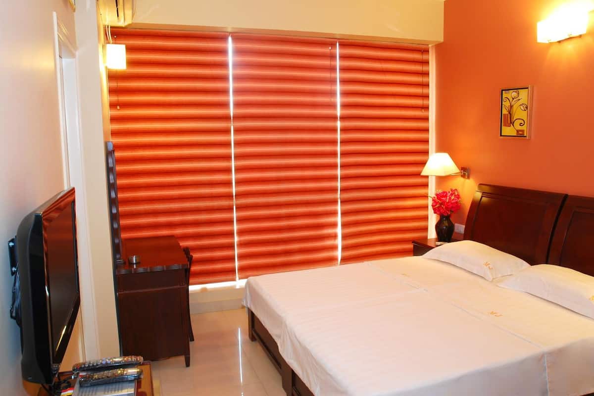 A hotel room with a bed, a TV, a nightstand, and a window with blinds.