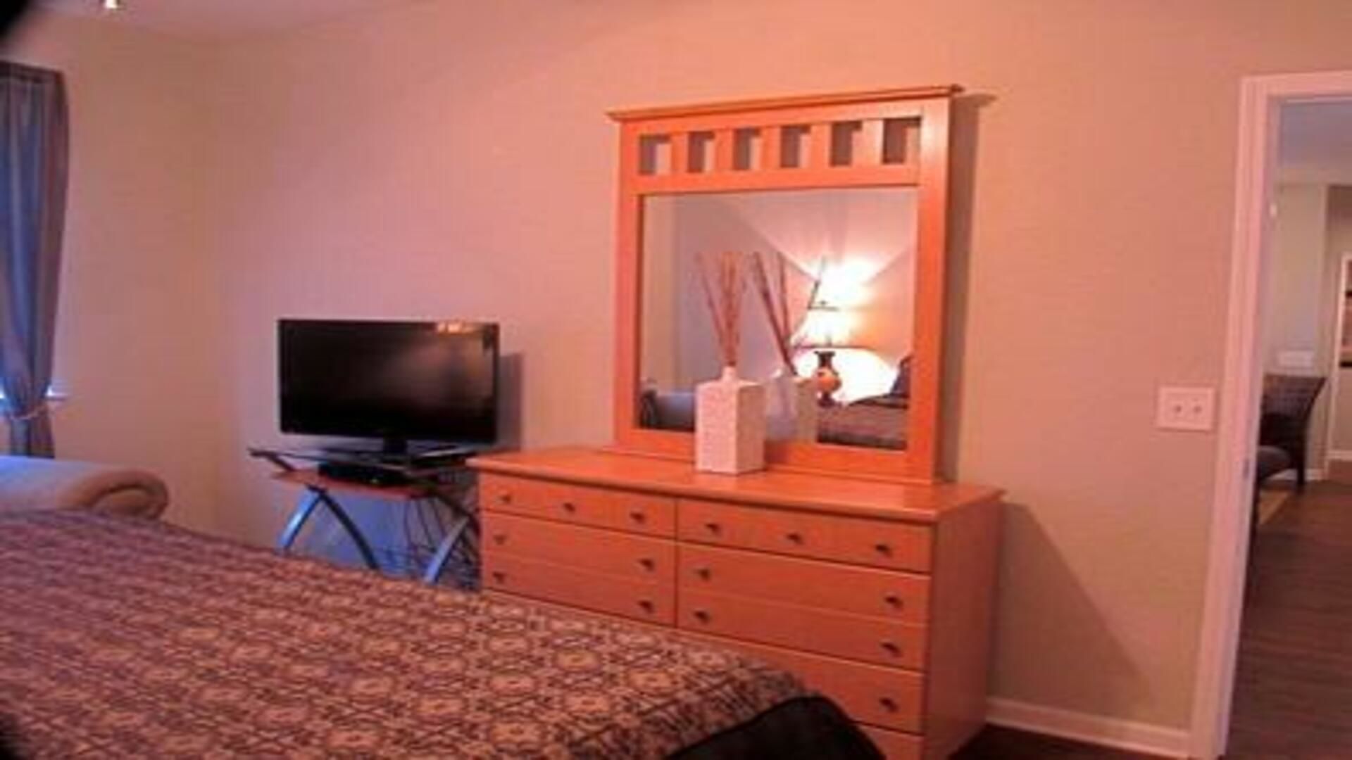 Quarto de hotel com cama, cómoda com gavetas, televisão e espelho.