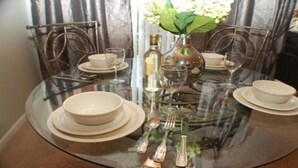 A round glass table set with white plates, bowls, wine glasses, and cutlery. A vase with flowers is placed in the center. - Tr603 - Terrace Ridge - 2 Bed 2 Baths Condo (Davenport)