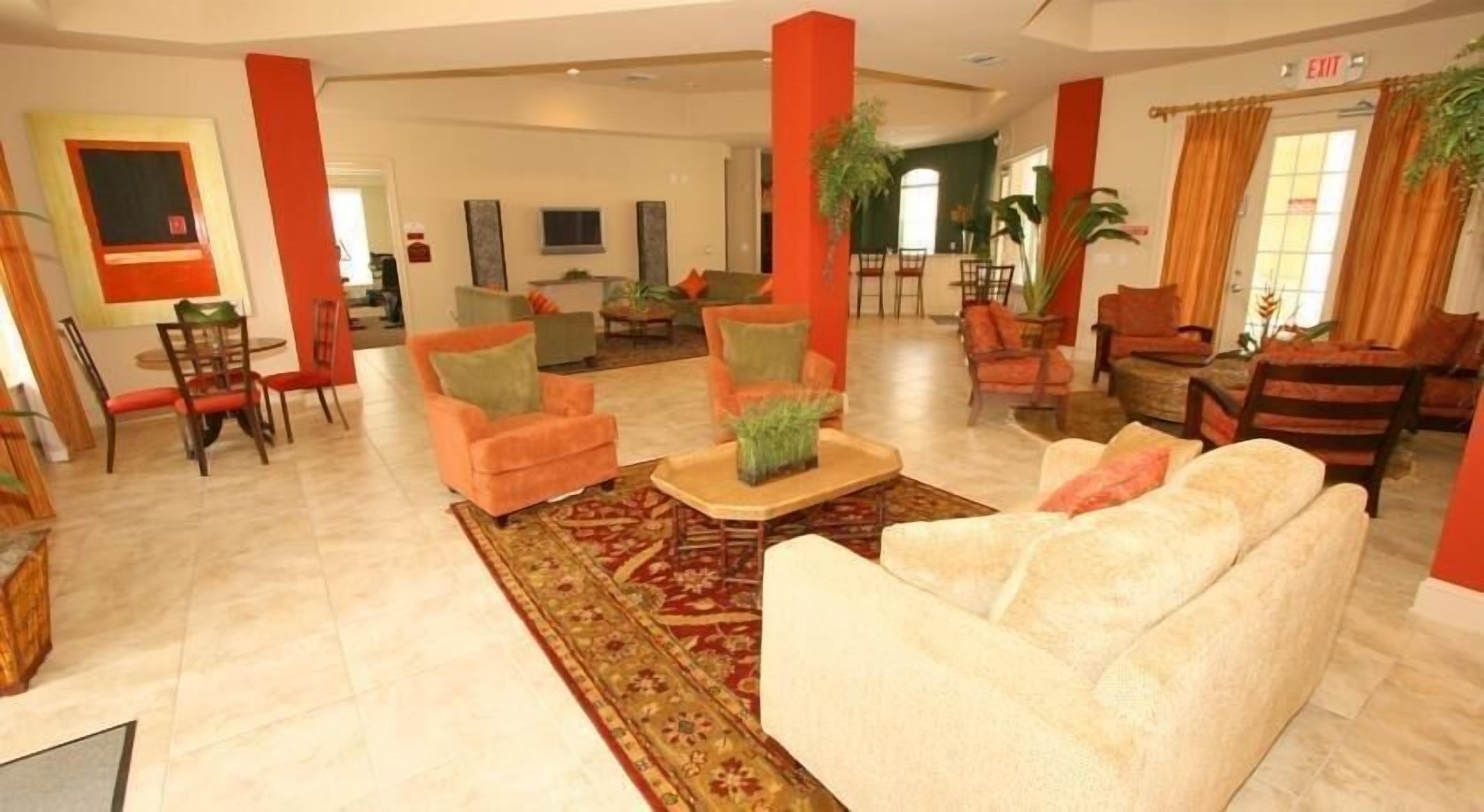 Un hall d’entrée spacieux avec un canapé blanc, des fauteuils orange et un mur d’accent rouge.
