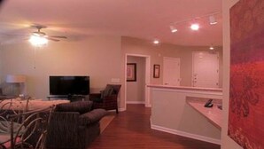 Una sala de estar con un televisor de pantalla plana, un ventilador de techo y un comedor con mesa y sillas.