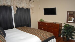 Une chambre d’hôtel avec un lit, une commode, une télévision et une plante en pot.