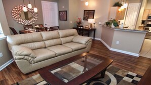 A living room with a beige sofa, a glass coffee table, and a wooden dining table. - Tr421 - Terrace Ridge - 2 Bed 2 Baths Condo (Davenport)
