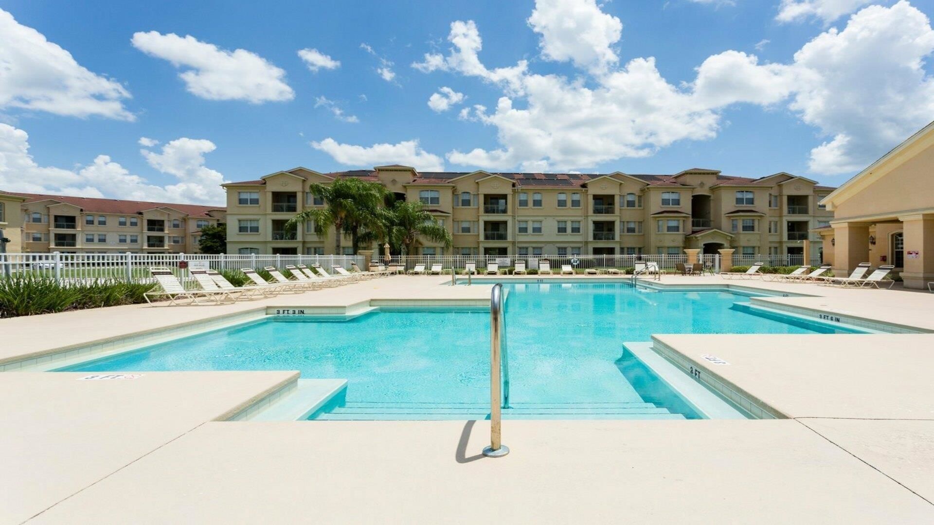 A rectangular pool with a diving board, surrounded by lounge chairs and a white fence.