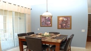 Een eetruimte met een tafel voor vier personen, omringd door stoelen. Boven de tafel hangen twee ingelijste foto's.