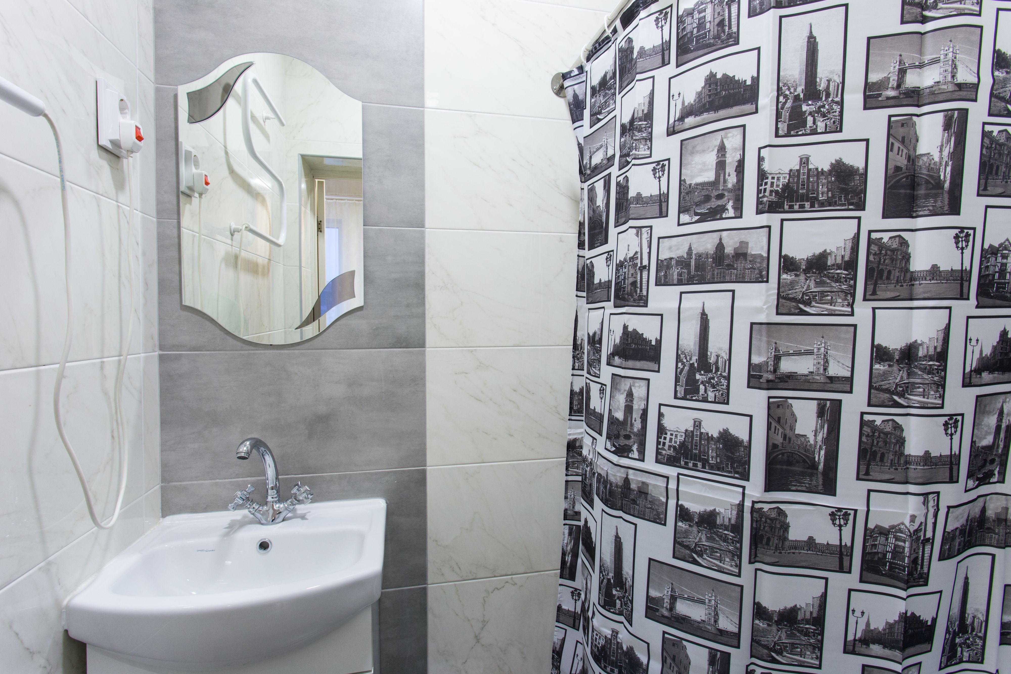 A bathroom with a white sink, a mirror, and a shower curtain with black and white cityscape photos.