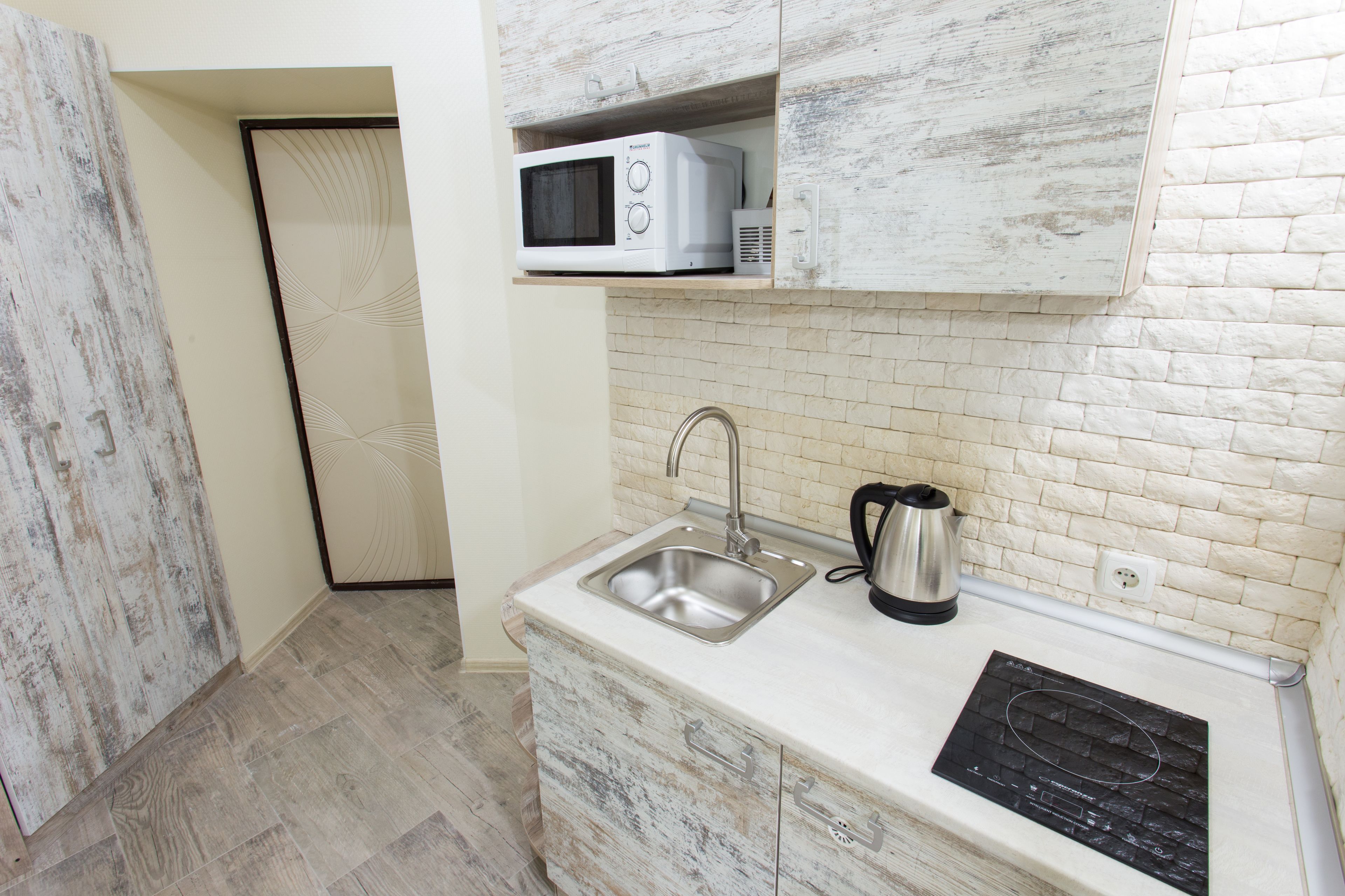 A compact kitchen with a microwave, sink, kettle, and a built-in stovetop.
