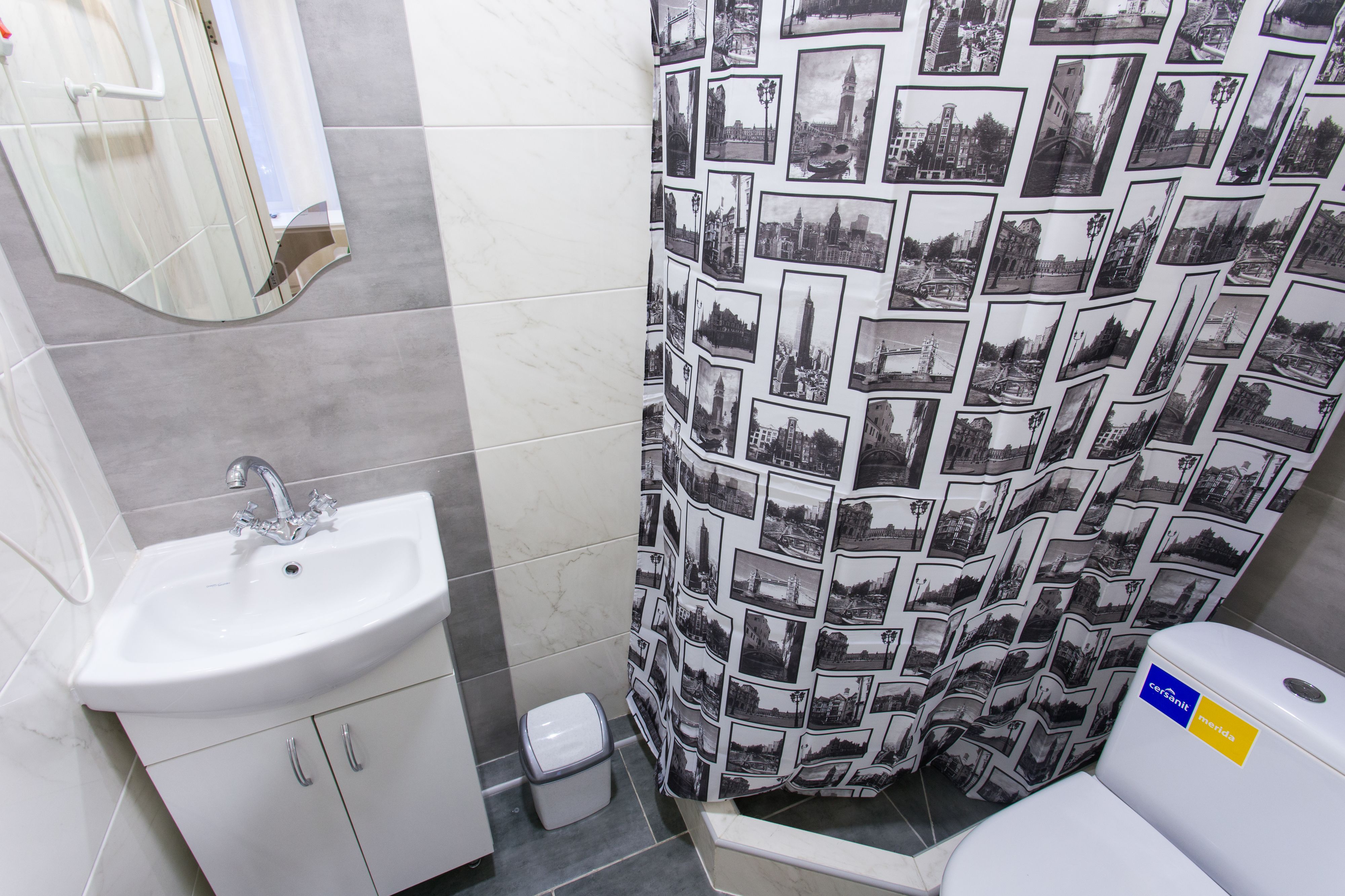 Un baño con lavamanos, inodoro y cortina de ducha con estampado de paisaje urbano.