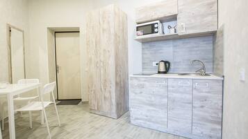 A compact kitchen with a white countertop, a microwave, and a sink. There is a white chair and a door leading to another room.