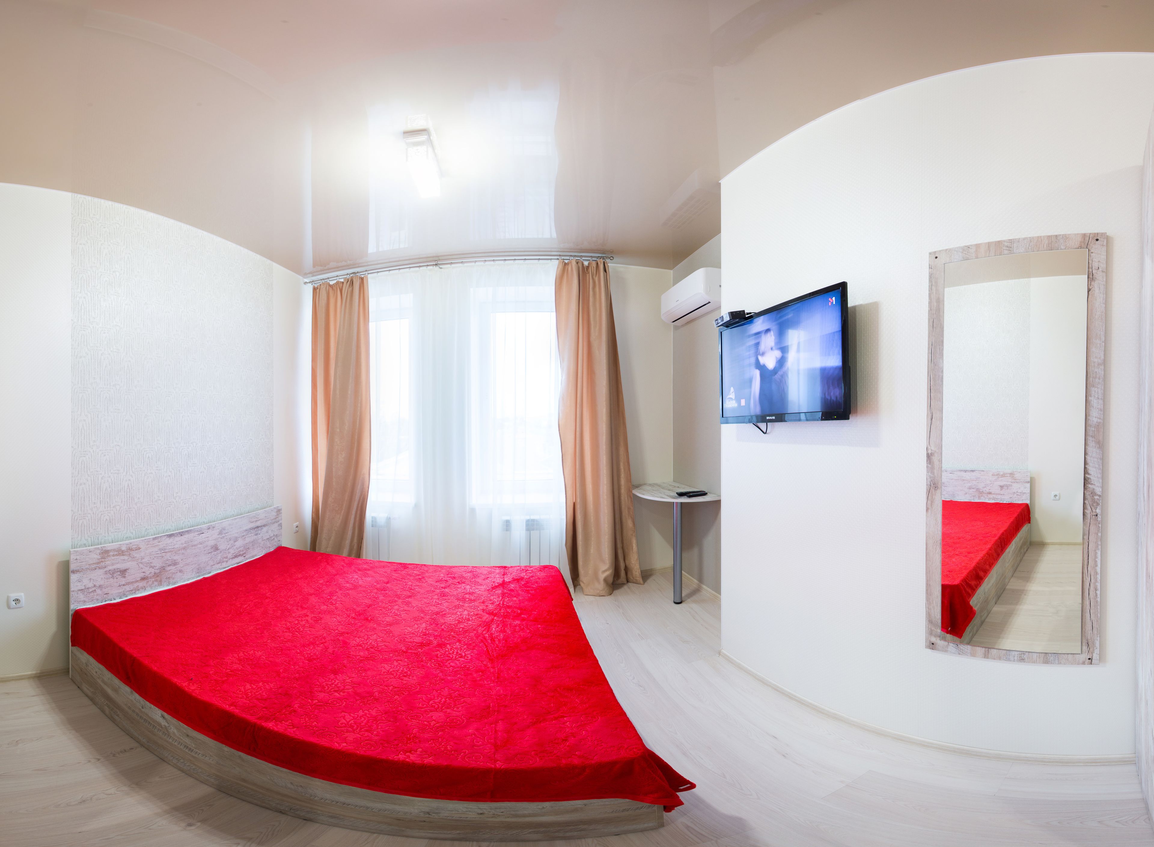 Un dormitorio con cama, televisión, espejo y ventana con cortinas.