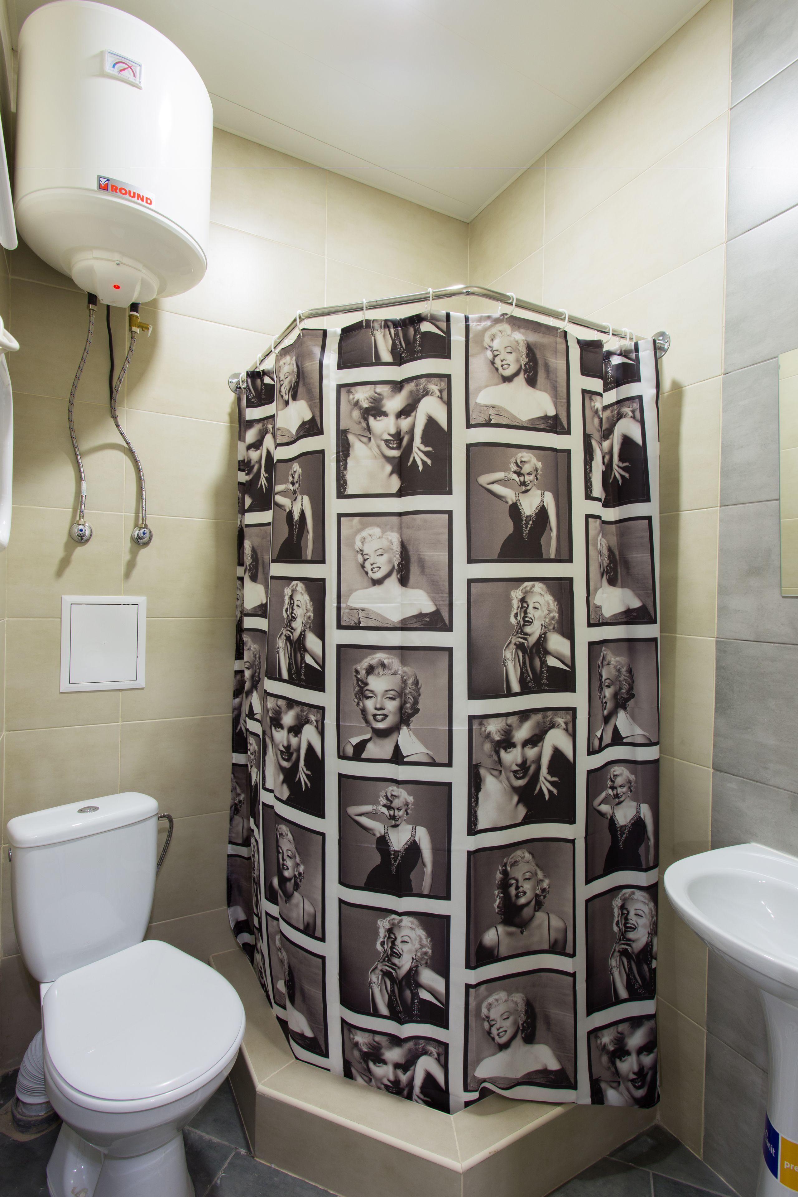 A bathroom with a shower curtain featuring a collage of Marilyn Monroe photos, a toilet, and a sink.