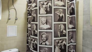 Un baño con cortina de ducha que muestra un collage de fotografías de Marilyn Monroe, un inodoro y un lavabo.