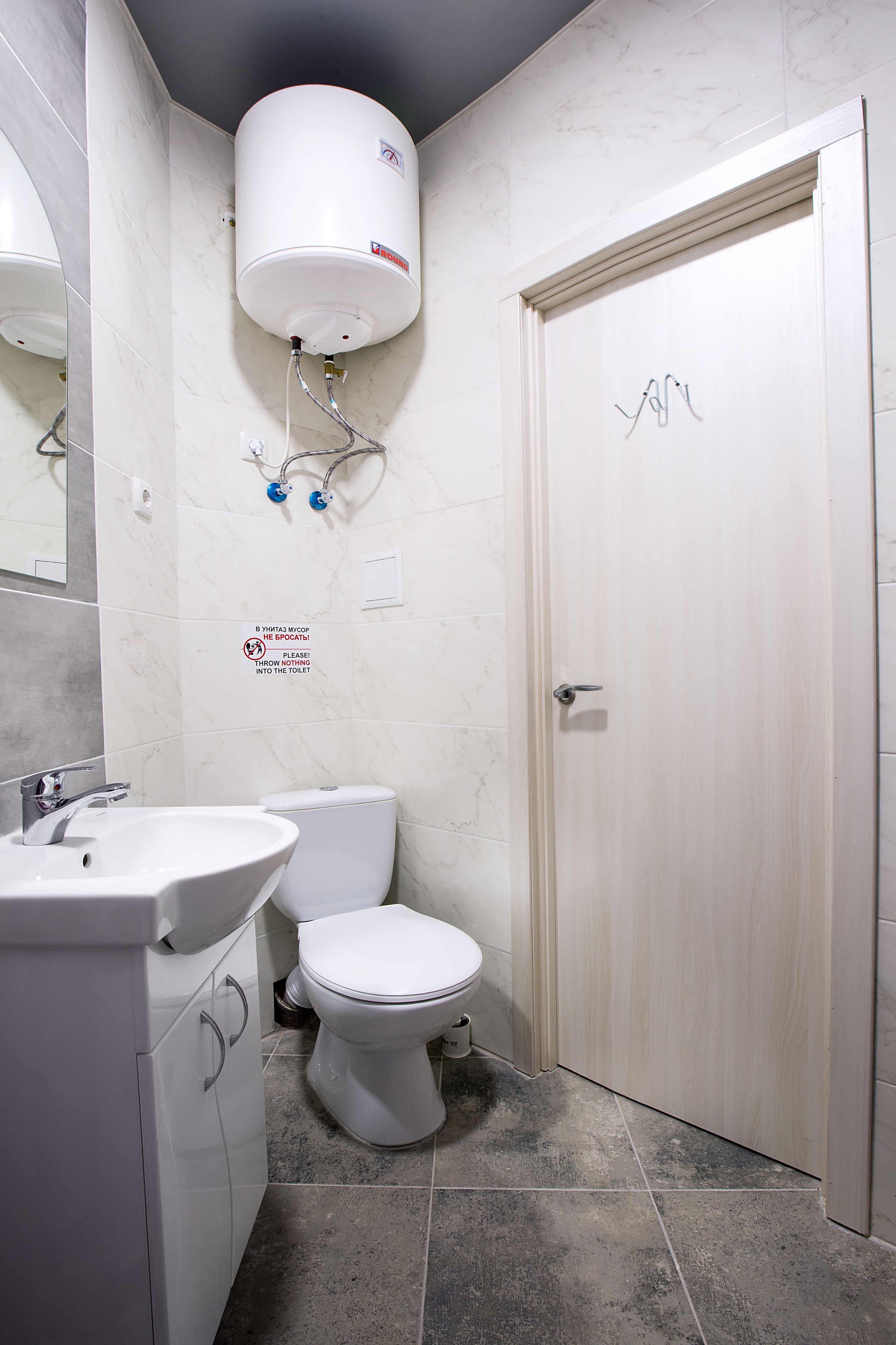 A bathroom with a white sink, toilet, and a water heater mounted on the wall.