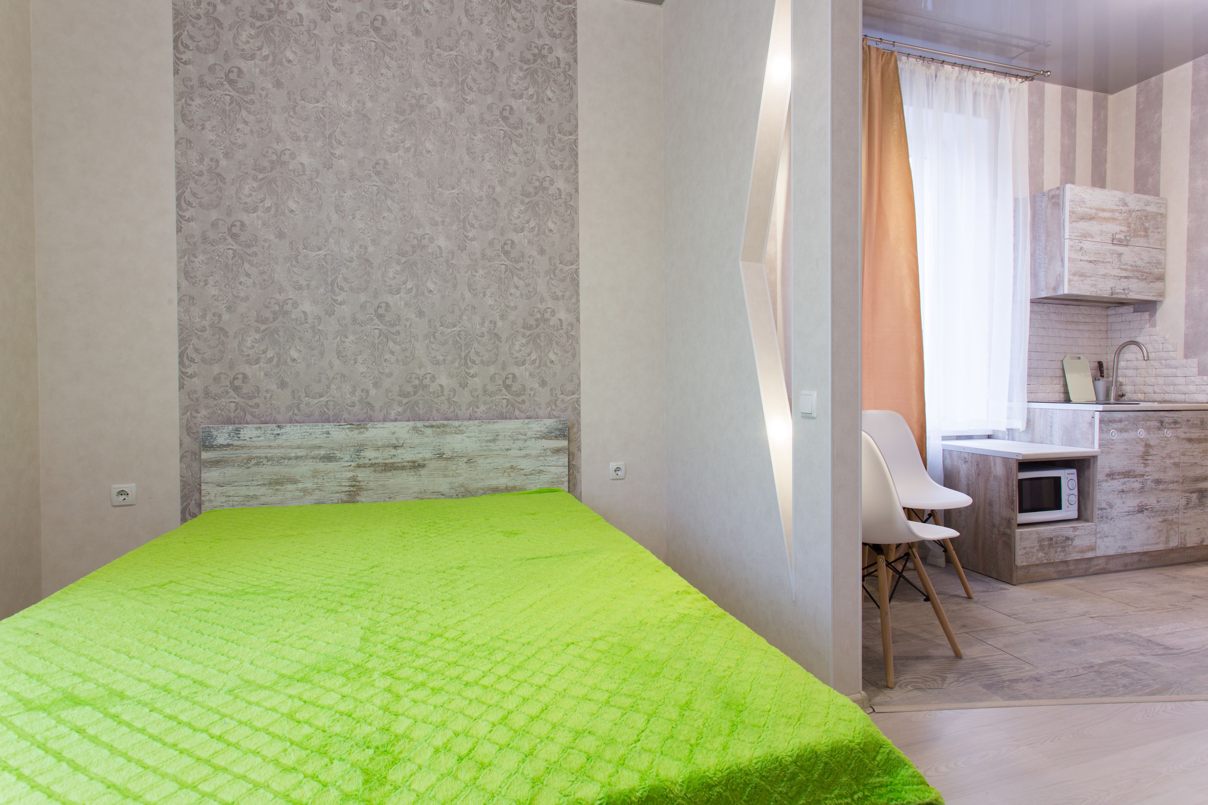 A room with a bed, a chair, a small kitchenette, and a bathroom with a shower curtain.
