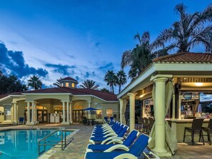 A pool area with lounge chairs, a bar, and a building with a red-tiled roof. - Ei2809 - Emerald Island - 6 Bed 6 Baths Villa (Kissimmee)