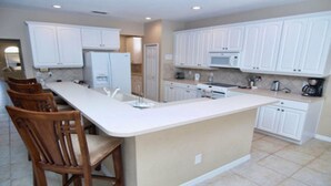 A kitchen with white cabinets, a central island, and a dining area with wooden chairs. - Ws305 - Watersong - 5 Bed 5 Baths Villa (Davenport)