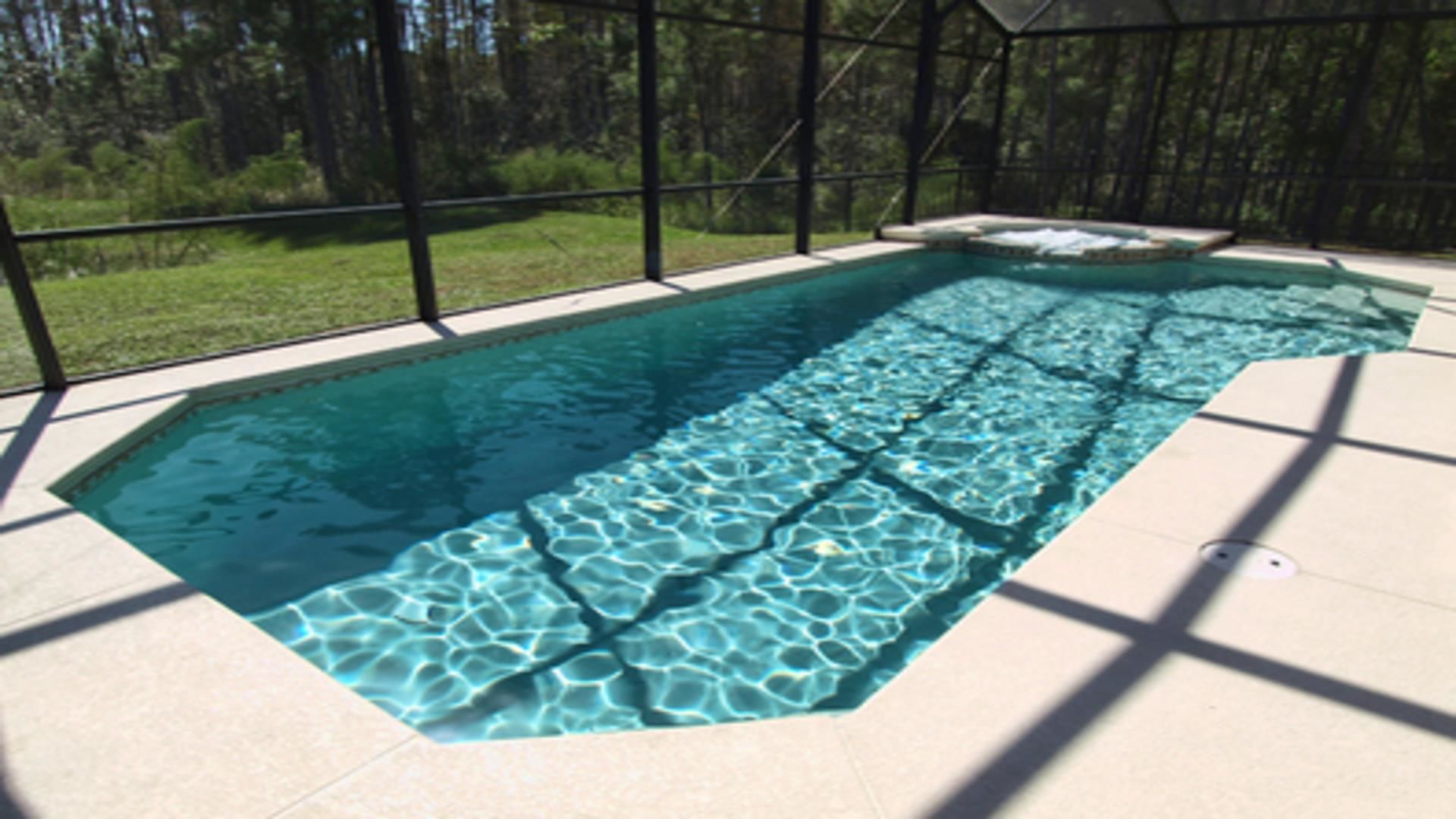 Une piscine rectangulaire à l’eau claire, entourée d’une structure en verre et bordée d’une terrasse carrelée.