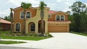 A two-story house with a red-tiled roof, a garage, and a front yard with palm trees. - Ws305 - Watersong - 5 Bed 5 Baths Villa (Davenport)
