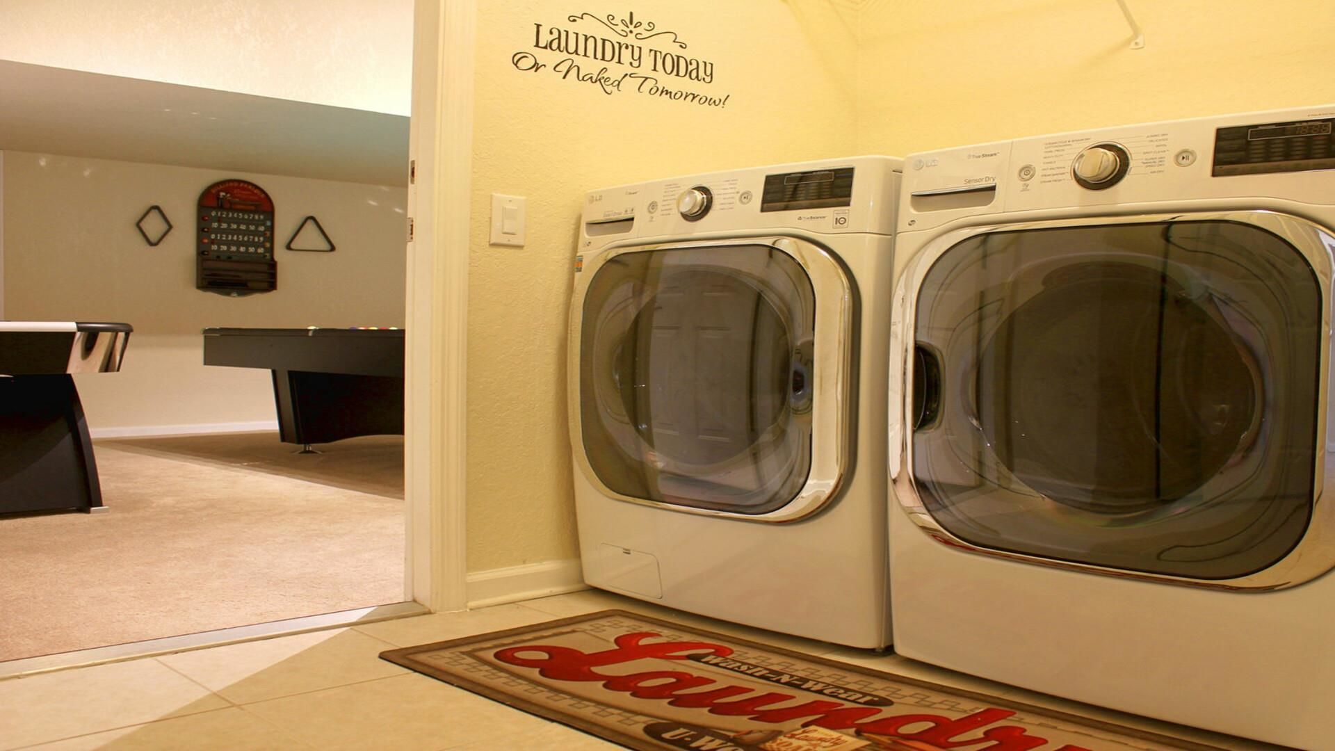 A laundry room with two front-loading washers, a wall-mounted drying rack, and a door mat with 'Laundry' written on it.