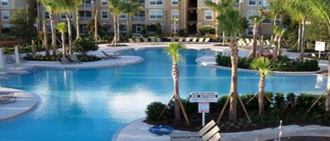 A resort pool area with multiple water features, lounge chairs, and palm trees.