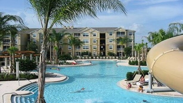 Ein Resort mit großem Pool, umgeben von Palmen und einem mehrstöckigen Gebäude mit Balkonen.