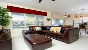 Ein geräumiges Wohnzimmer mit braunem Ledersofa, passendem Hocker und einer Essecke mit Stuhl und Tisch.