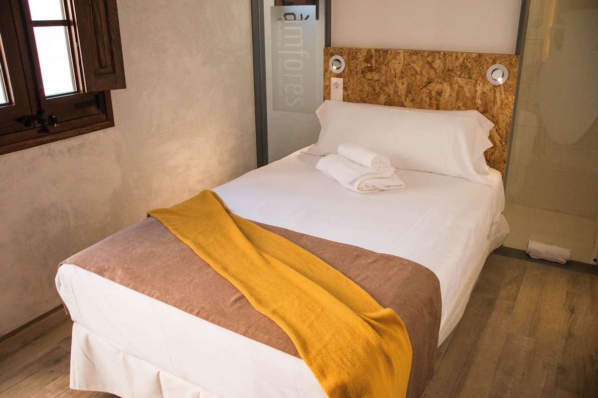 Ein ordentlich gemachtes Bett mit einer braun-weißen Tagesdecke, einer gelben Decke und sauber gefalteten weißen Handtüchern.