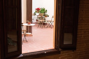 Abertura de porta que dá para um pátio com mesa, cadeiras e vasos de plantas.