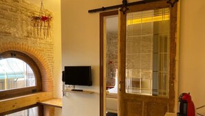 A cozy room with a wooden bench, a television, a sliding door, and a coffee station. - Amfores Boutique Guest House (Barcelona)